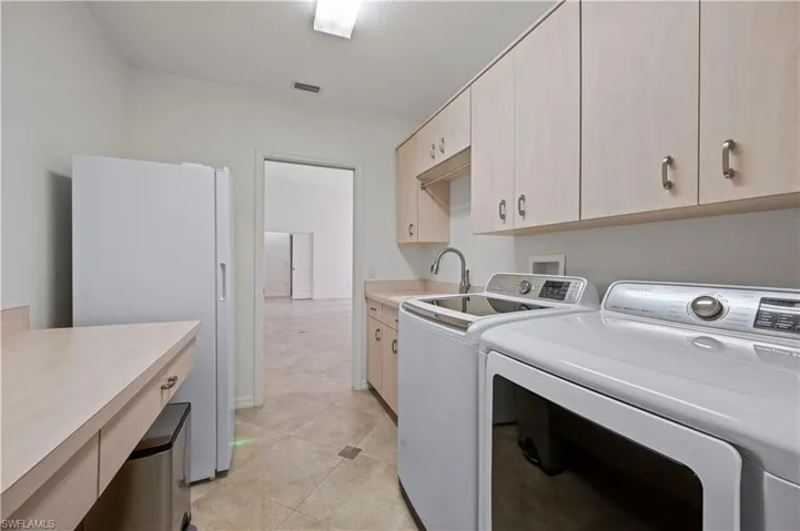 Clothes washing area with cabinets, washer and clothes dryer, sink, and light tile patterned floors
