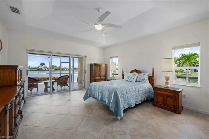Tiled bedroom with a tray ceiling, multiple windows, and access to exterior