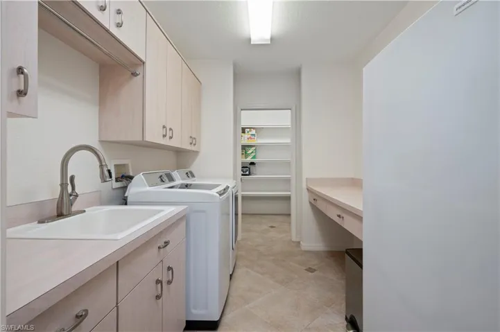 Laundry area with washing machine and clothes dryer, cabinets, and sink