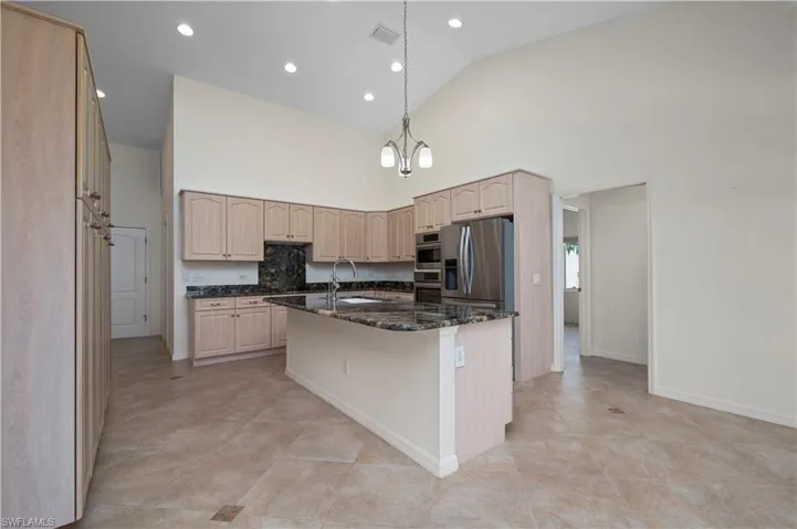 Kitchen with decorative light fixtures, a center island with sink, stainless steel appliances, high vaulted ceiling, and dark stone countertops