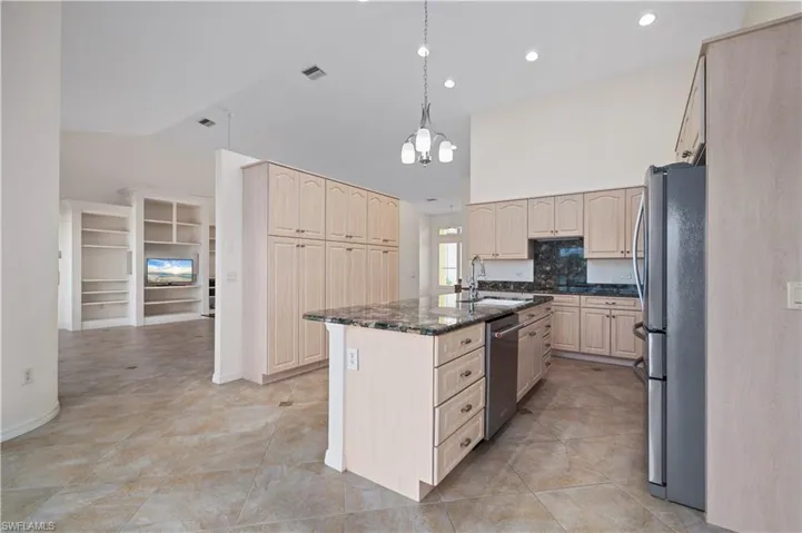 Kitchen with dark stone counters, pendant lighting, stainless steel appliances, sink, and a center island with sink