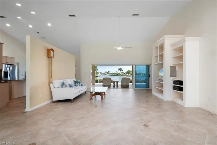 Tiled living room featuring built in features, ceiling fan, and high vaulted ceiling