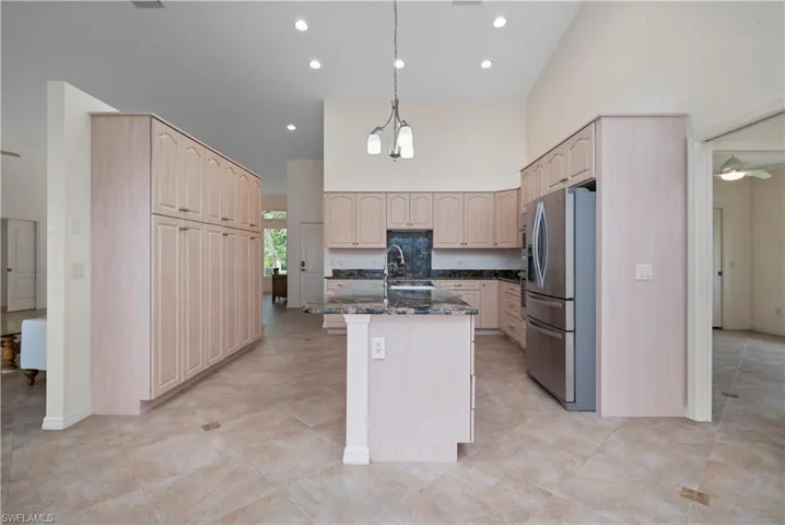 Kitchen featuring pendant lighting, ceiling fan with notable chandelier, stainless steel fridge, sink, and a center island with sink