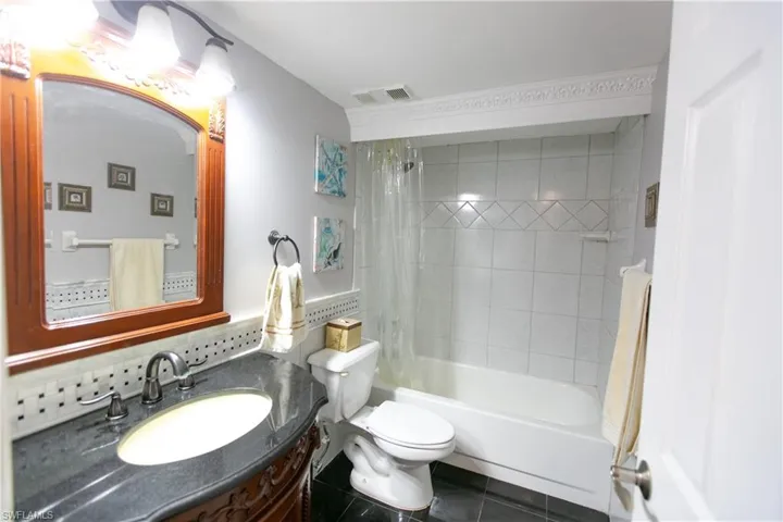 Full bath featuring shower / tub combo with curtain, vanity, dark tile patterned flooring, and decorative backsplash