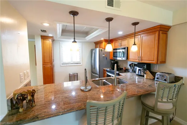 Kitchen featuring a raised ceiling, a peninsula, ornamental molding, stainless steel microwave, and a kitchen bar