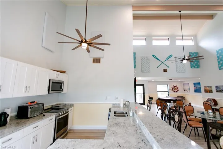 Kitchen with a ceiling fan, light stone countertops, appliances with stainless steel finishes, a high ceiling, and light wood finished floors