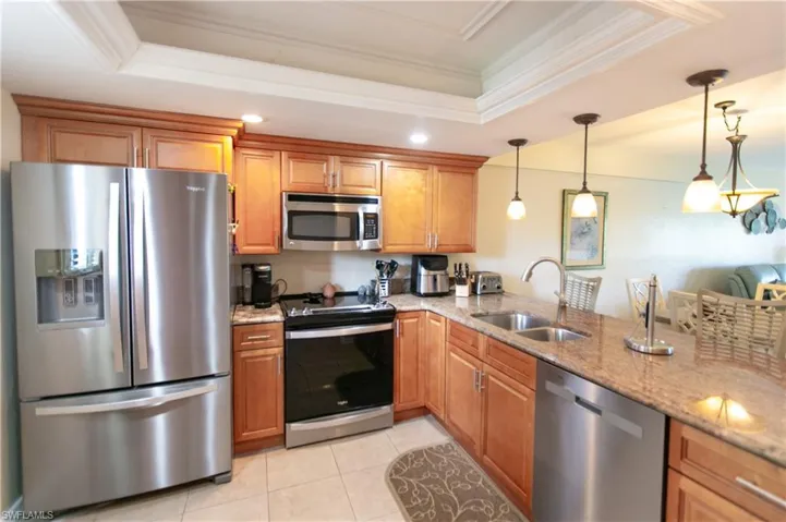 Kitchen with stainless steel appliances, light stone counters, a raised ceiling, ornamental molding, and brown cabinetry