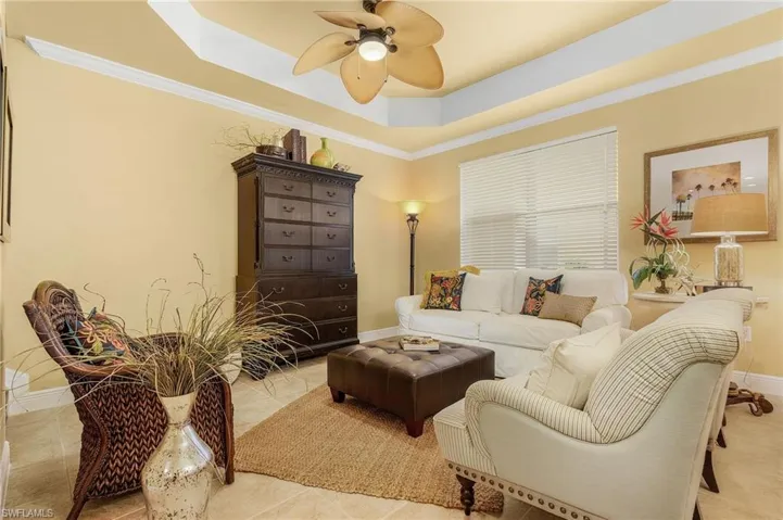 Living area with a ceiling fan, a tray ceiling, baseboards, ornamental molding, and light tile patterned flooring