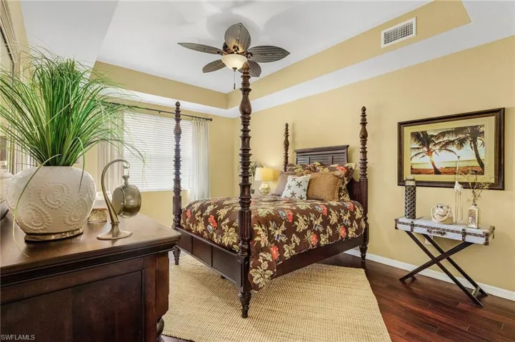 Bedroom with a ceiling fan, baseboards, dark wood finished floors, visible vents, and a raised ceiling