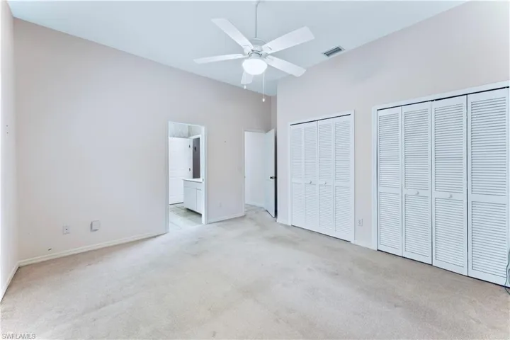 Unfurnished bedroom featuring ceiling fan, two closets, light colored carpet, and ensuite bath
