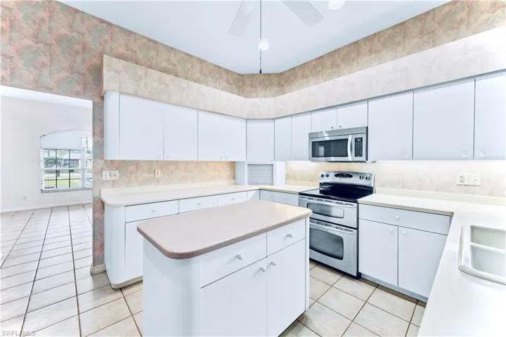 Kitchen featuring light tile patterned floors, ceiling fan, stainless steel appliances, white cabinets, and a kitchen island