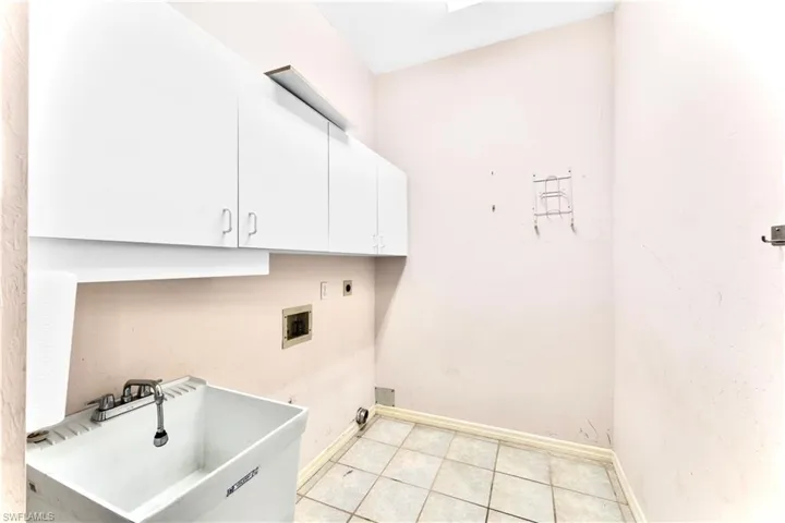 Washroom with light tile patterned flooring, sink, cabinets, hookup for a washing machine, and electric dryer hookup
