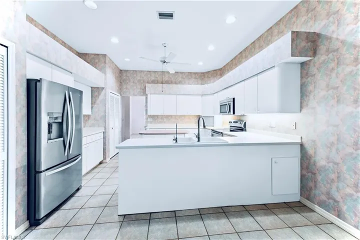Kitchen with appliances with stainless steel finishes, sink, white cabinets, light tile patterned floors, and kitchen peninsula