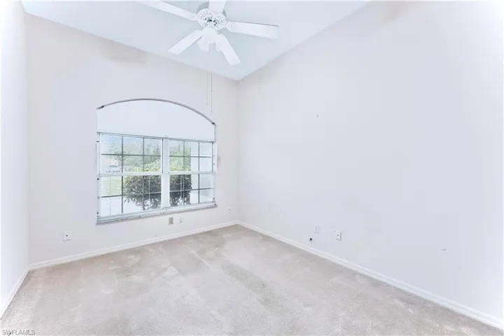 Empty room with high vaulted ceiling, light colored carpet, and ceiling fan