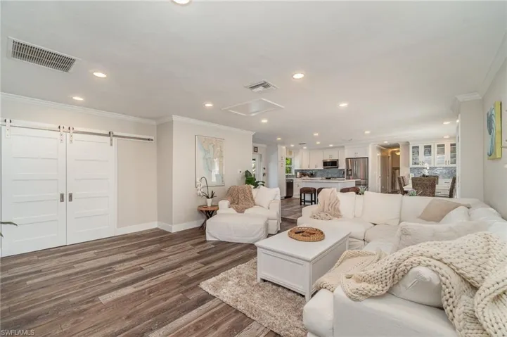 Living room featuring crown molding, a barn door, recessed lighting, and dark wood-style floors