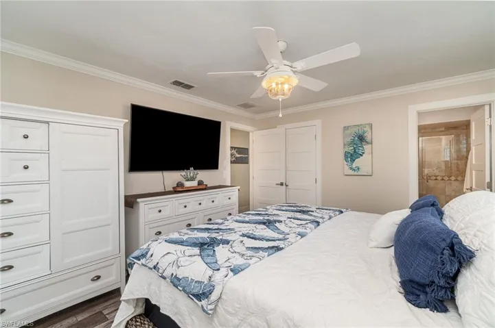 Bedroom featuring ornamental molding, dark wood-style floors, a ceiling fan, and ensuite bath
