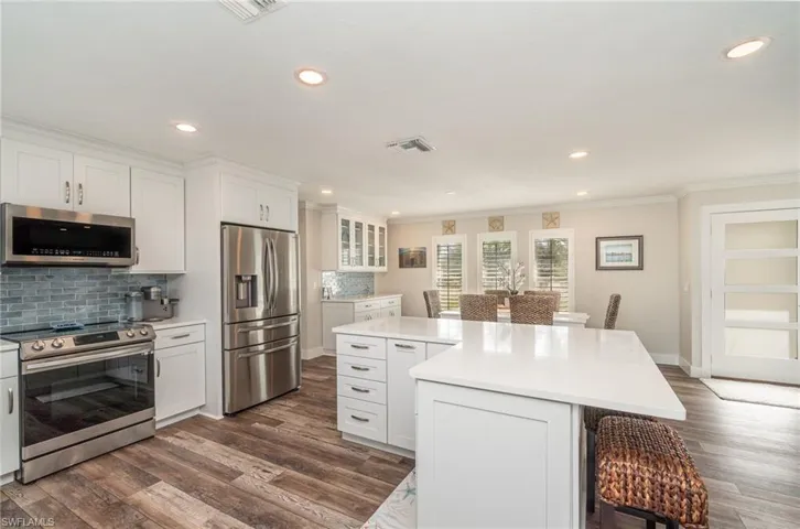 Kitchen with appliances with stainless steel finishes, a kitchen breakfast bar, white cabinetry, glass insert cabinets, and recessed lighting
