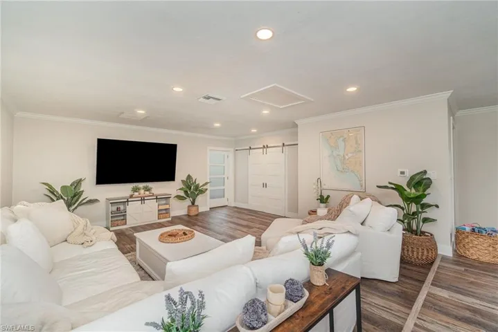 Living room with recessed lighting, attic access, wood finished floors, a barn door, and crown molding