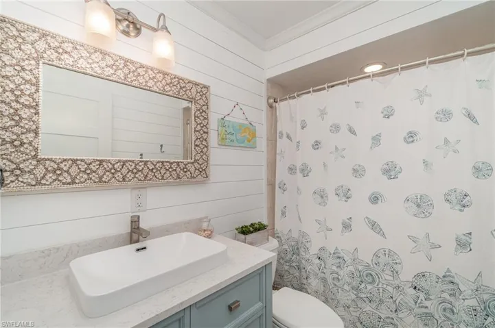 Full bathroom with vanity, a shower with shower curtain, wooden walls, and crown molding
