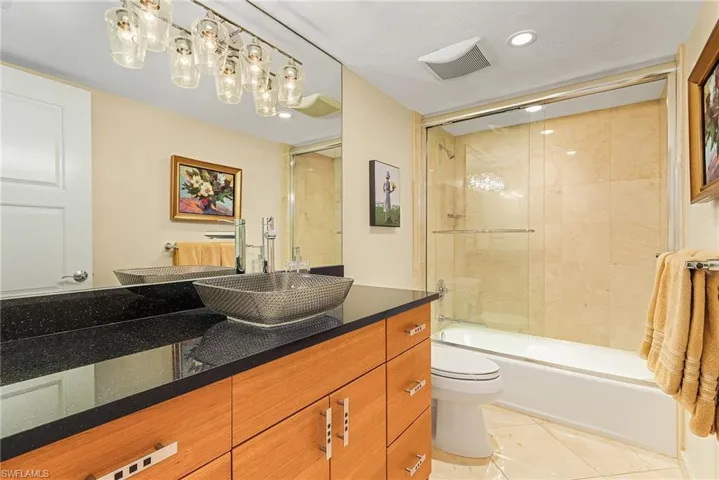 Full bathroom with toilet, tile patterned floors, vanity, and enclosed tub / shower combo