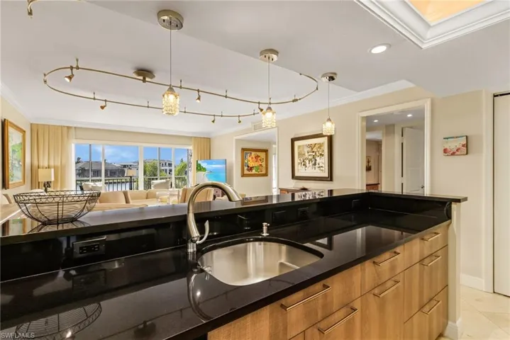 Kitchen with ornamental molding, decorative light fixtures, light tile patterned floors, sink, and dark stone countertops