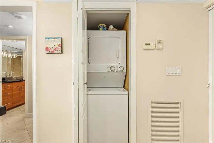Laundry area featuring light tile patterned floors, sink, and stacked washer / dryer