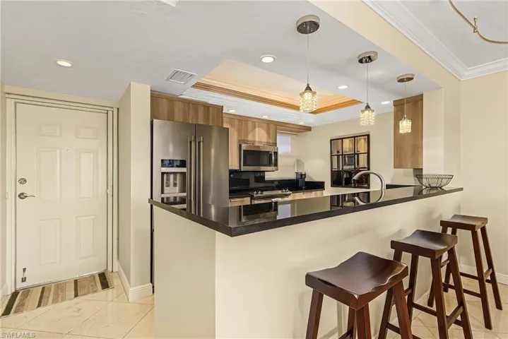 Kitchen featuring stainless steel appliances, kitchen peninsula, pendant lighting, a breakfast bar area, and a tray ceiling