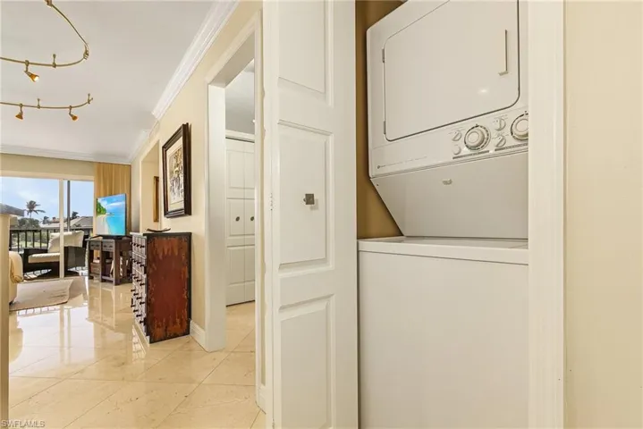 Laundry area with light tile patterned flooring, stacked washer / dryer, and crown molding