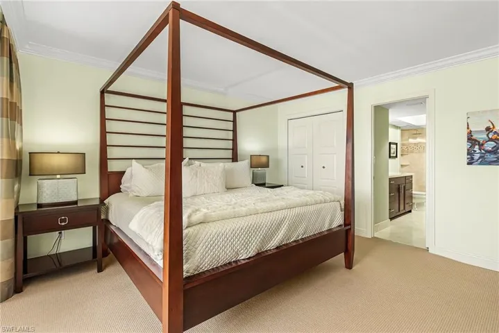 Bedroom with a closet, light colored carpet, crown molding, and ensuite bath