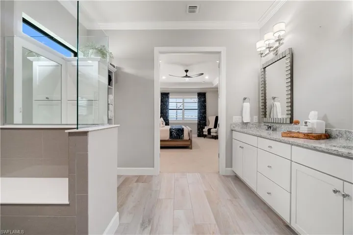Bathroom featuring a tray ceiling, hardwood / wood-style floors, ceiling fan, ornamental molding, and double sink vanity