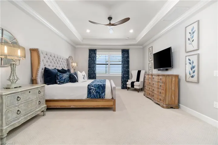 Bedroom with ornamental molding, carpet flooring, ceiling fan, and a tray ceiling