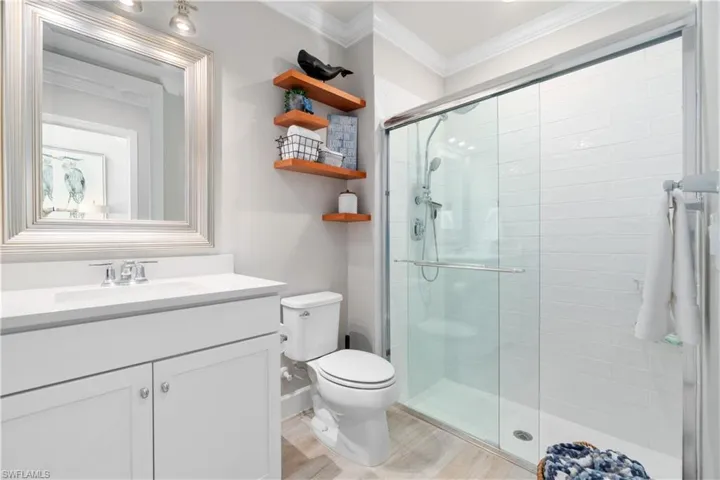 Bathroom with a shower with door, crown molding, toilet, and vanity