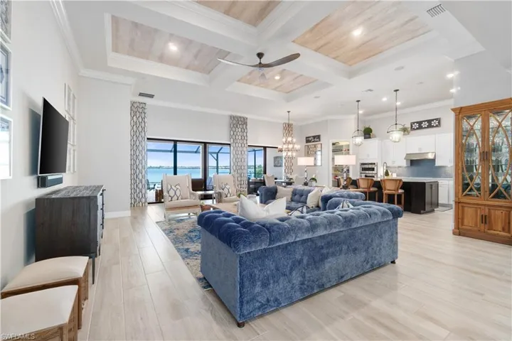 Living room featuring beamed ceiling, light hardwood / wood-style flooring, ceiling fan with notable chandelier, ornamental molding, and coffered ceiling