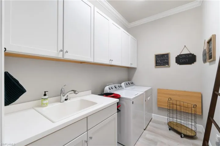 Laundry area featuring light wood-type flooring, washer and dryer, cabinets, sink, and ornamental molding