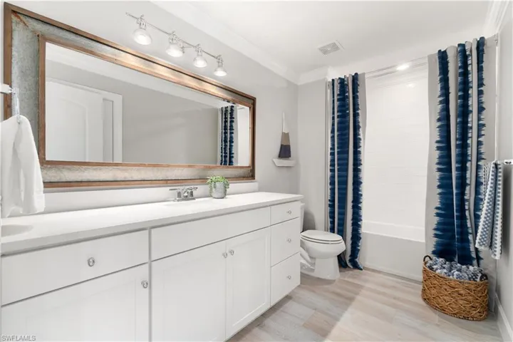 Full bathroom featuring shower / bathtub combination with curtain, toilet, vanity, hardwood / wood-style flooring, and ornamental molding