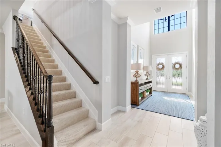 Entrance foyer with a towering ceiling, french doors, light wood-type flooring, and crown molding