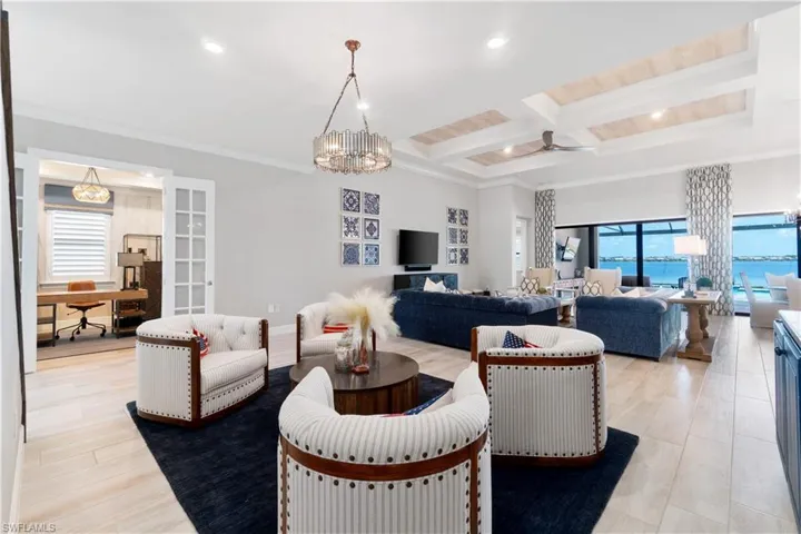 Living room featuring ceiling fan with notable chandelier, ornamental molding, beamed ceiling, coffered ceiling, and light hardwood / wood-style flooring