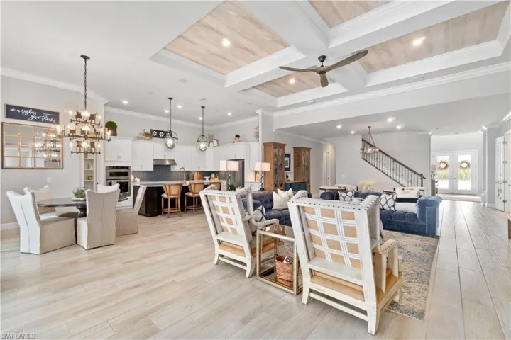 Living room featuring ornamental molding, beam ceiling, coffered ceiling, and ceiling fan with notable chandelier