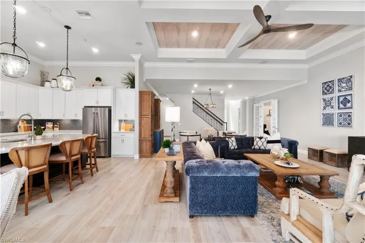 Living room with ceiling fan with notable chandelier, crown molding, light wood-type flooring, sink, and coffered ceiling