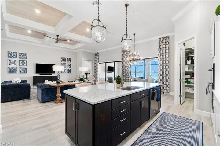 Kitchen featuring light hardwood / wood-style flooring, hanging light fixtures, coffered ceiling, a center island with sink, and ornamental molding