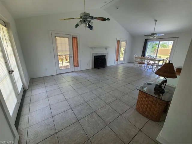 Living room featuring a ceiling fan, a fireplace, high vaulted ceiling, light tile patterned floors, and beam ceiling