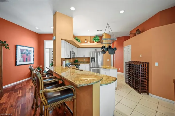 Kitchen featuring white cabinets, light stone countertops, stainless steel appliances, kitchen peninsula, and a kitchen breakfast bar