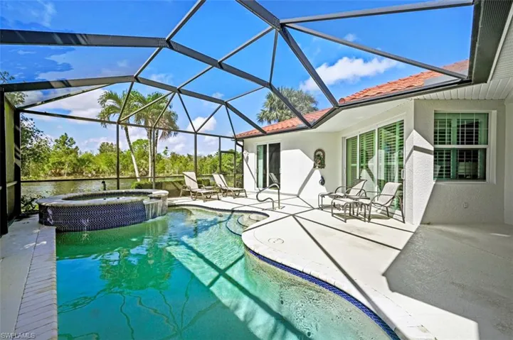 View of pool with a water view, glass enclosure, a patio area, and an in ground hot tub