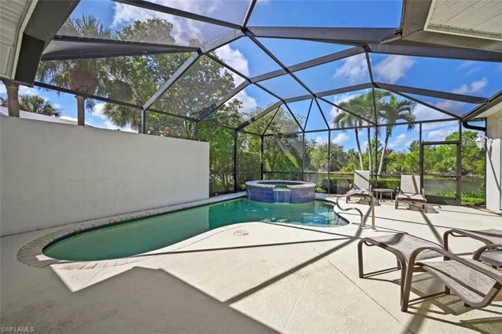 View of swimming pool featuring glass enclosure, an in ground hot tub, a water view, and a patio