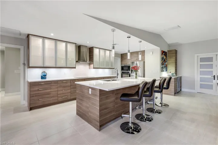 Kitchen featuring wall chimney range hood, sink, backsplash, a kitchen breakfast bar, and a large island