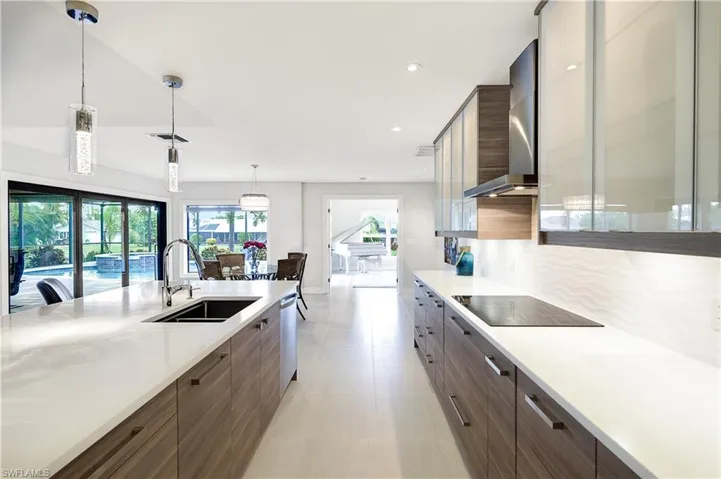 Kitchen with black electric stovetop, wall chimney range hood, sink, hanging light fixtures, and stainless steel appliances