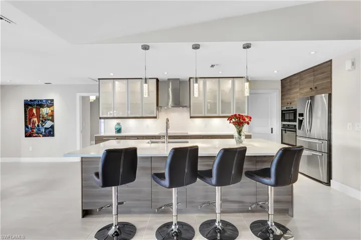 Kitchen featuring wall chimney range hood, stainless steel appliances, vaulted ceiling, and a kitchen island with sink