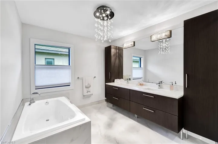Primary Bathroom featuring vanity, a chandelier, tiled bath, and a wealth of natural light