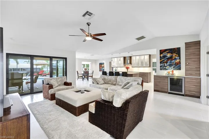 Living room with ceiling fan, light tile patterned floors, vaulted ceiling, and beverage cooler