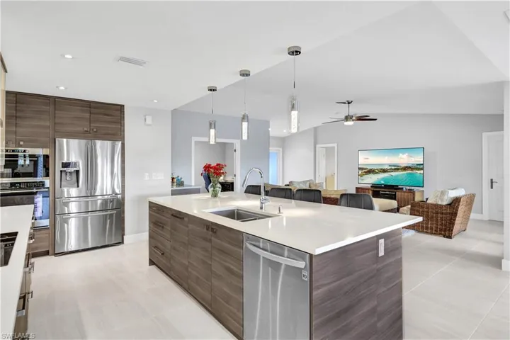 Kitchen featuring stainless steel appliances, vaulted ceiling, decorative light fixtures, and a center island with sink